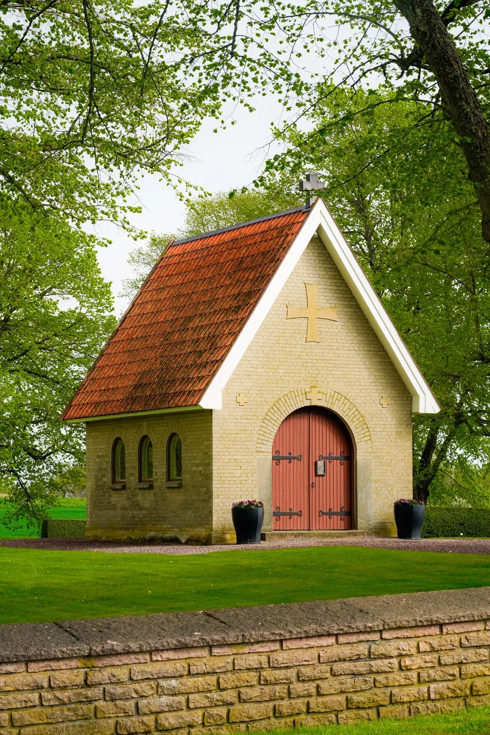 A small brick chapel with a red-tiled roof and a cross